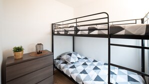 Un lit superposé avec une couvre-lit à motifs géométriques, une petite table de chevet avec un panier en osier et une bougie, et un mur sobre.