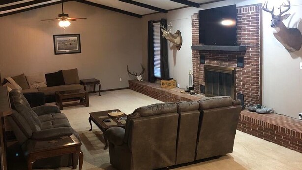 A living room with a fireplace, a ceiling fan, and a mounted deer head. - Stuttgart Lodge (Stuttgart)