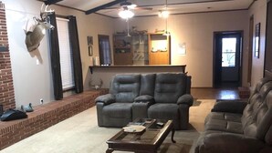 A spacious living room with a high ceiling, exposed beams, and a fireplace. There are two leather sofas, a glass coffee table, and a deer head mounted on the wall. - Stuttgart Lodge (Stuttgart)
