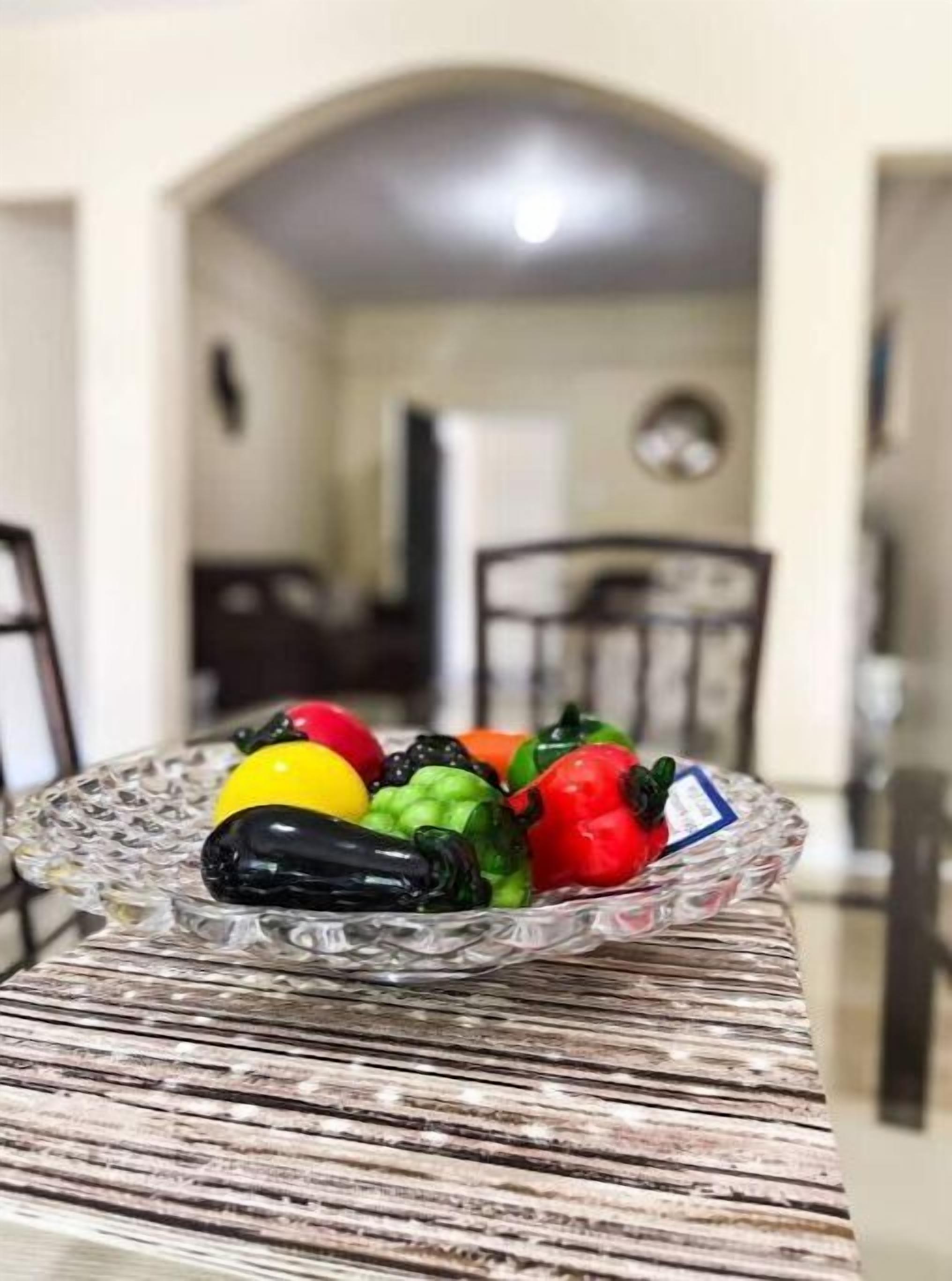 Un cuenco de vidrio con pimientos de colores sobre una mesa de madera en un comedor.