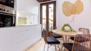 A modern kitchen with white cabinets, a stainless steel oven, and a dining area with wicker chairs and a wooden table. - Genteel Home Santas Patronas II (Seville)