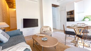 A modern living room with a flat-screen TV, a wooden coffee table, and a dining area with a round table and chairs. - Genteel Home Santas Patronas II (Seville)