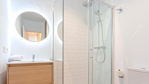 A modern bathroom with a glass-enclosed shower, a round mirror, and a wooden vanity. - Genteel Home Santas Patronas III (Seville)