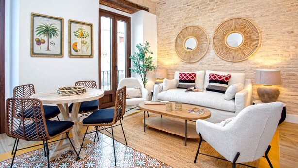 A living room with a round coffee table, white sofa, and wicker chairs. There are two framed botanical prints on the wall. - Genteel Home Santas Patronas III (Seville)