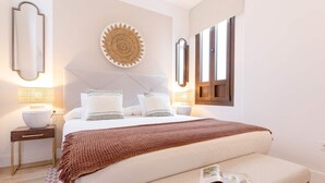 A neatly arranged bedroom with a large bed, bedside tables, a wall-mounted mirror, and a decorative plate. - Genteel Home Santas Patronas III (Seville)