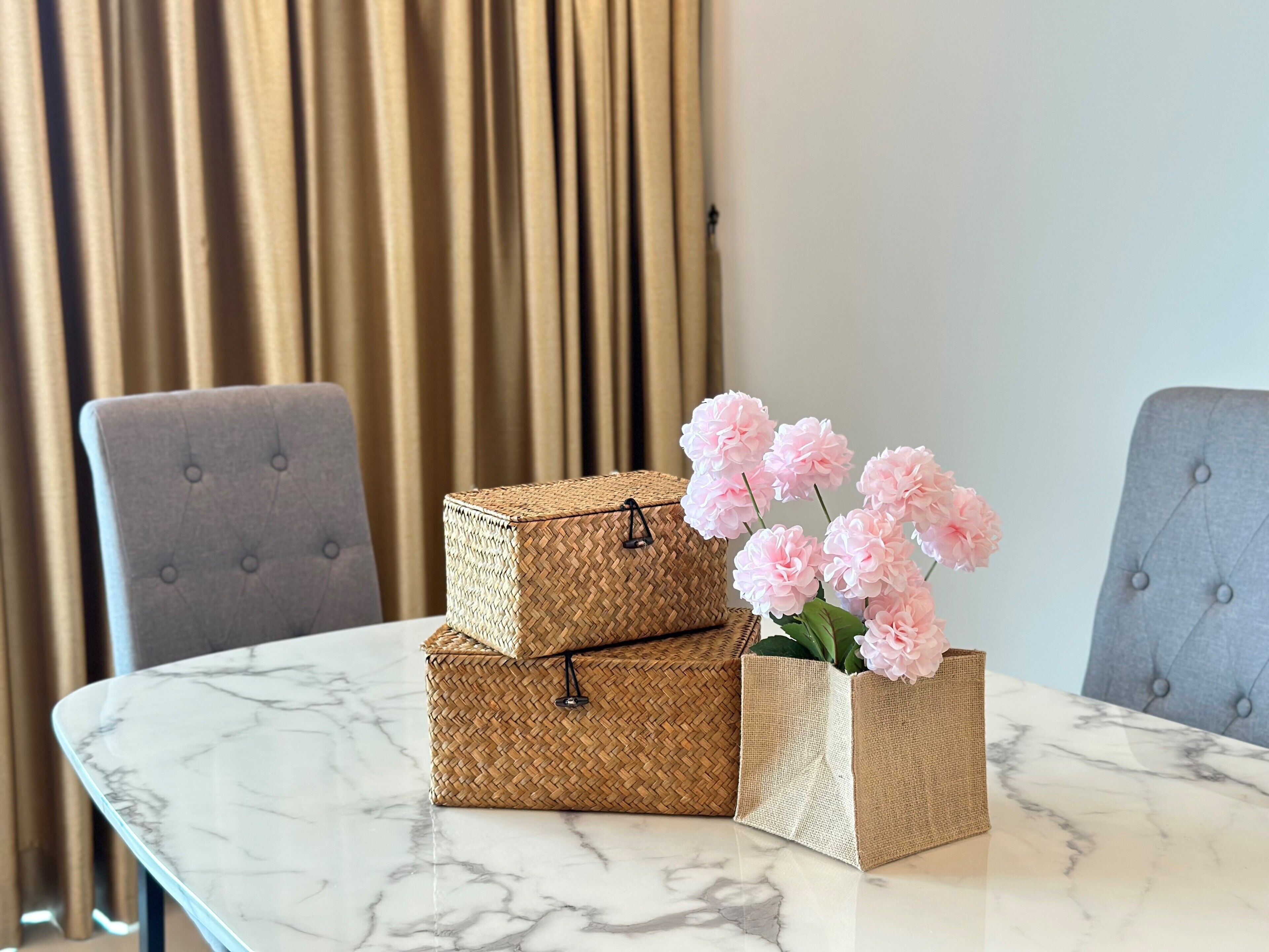 A table with two woven baskets and a vase with pink flowers.