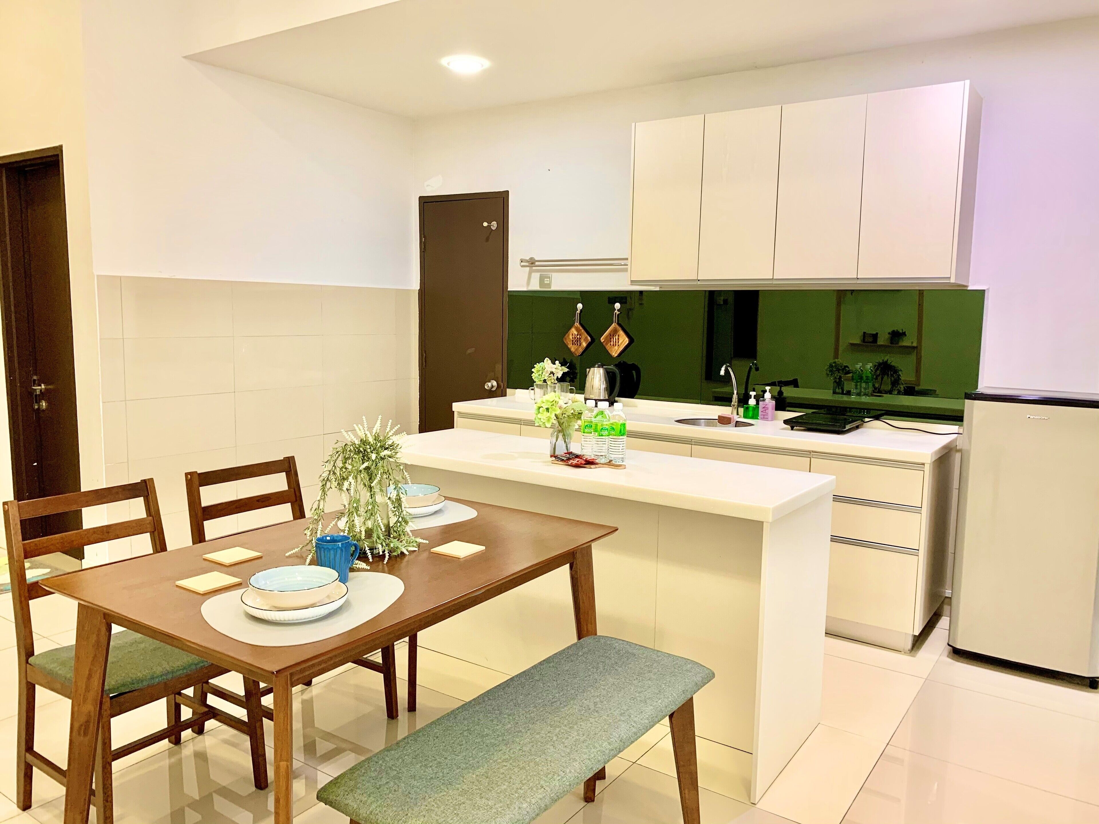 Una cocina moderna con armarios blancos, una isla integrada y un comedor con mesa y sillas de madera.