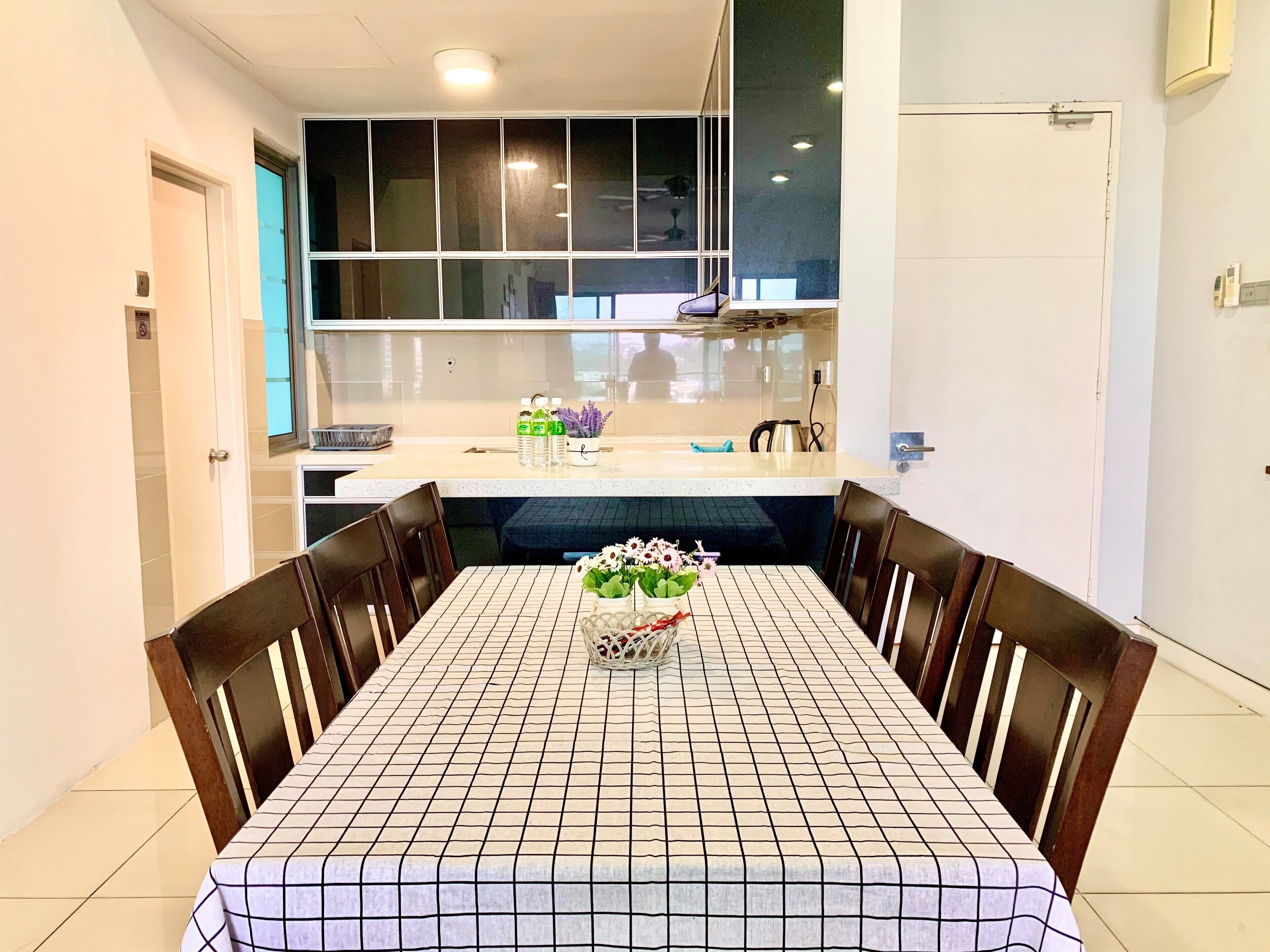 A dining area with a tiled table and chairs, a kitchen in the background, and a door on the left.