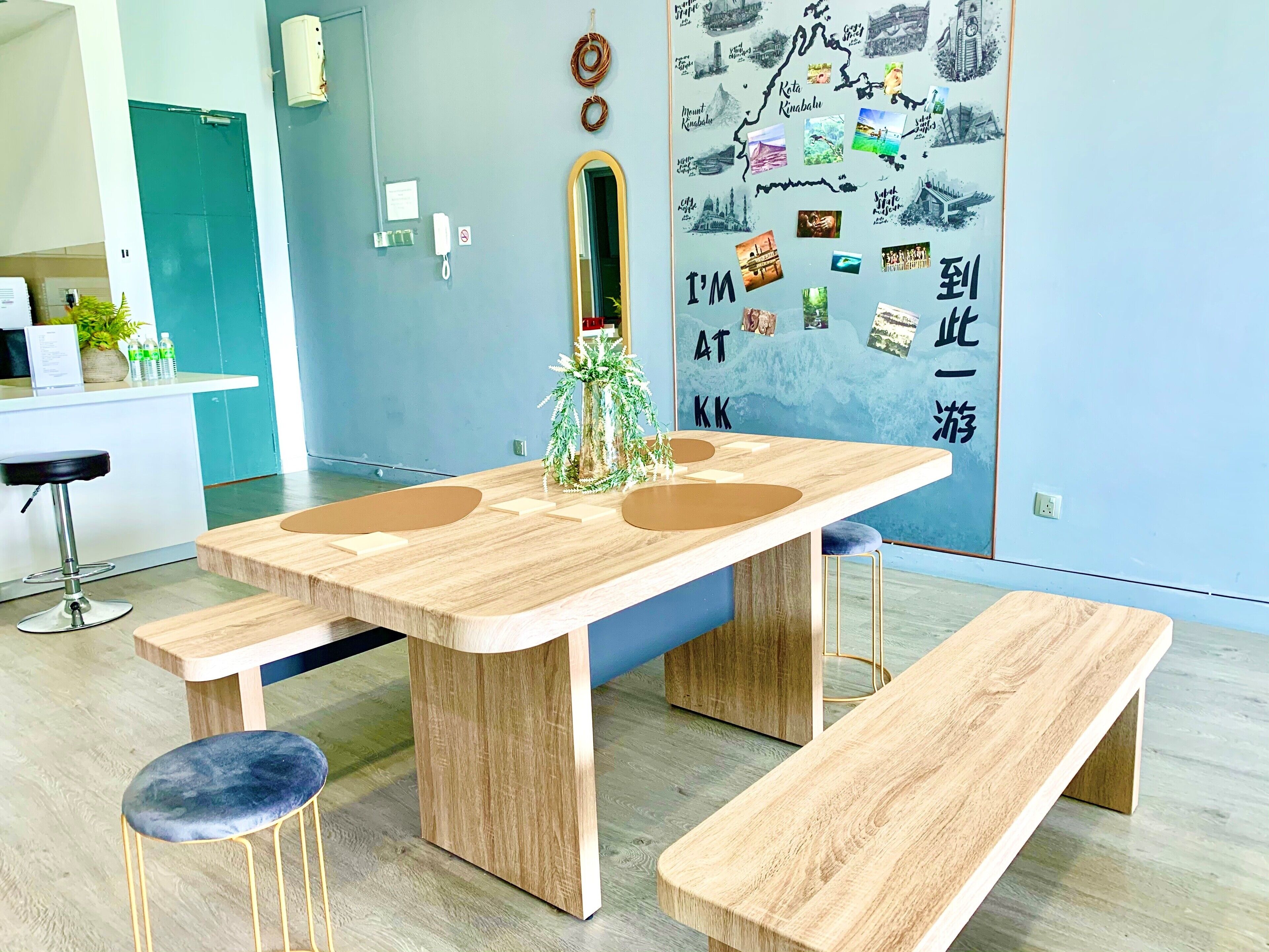 Un espace repas moderne avec une table et des bancs en bois, une petite plante en pot et un mur décoré sur le thème du voyage.