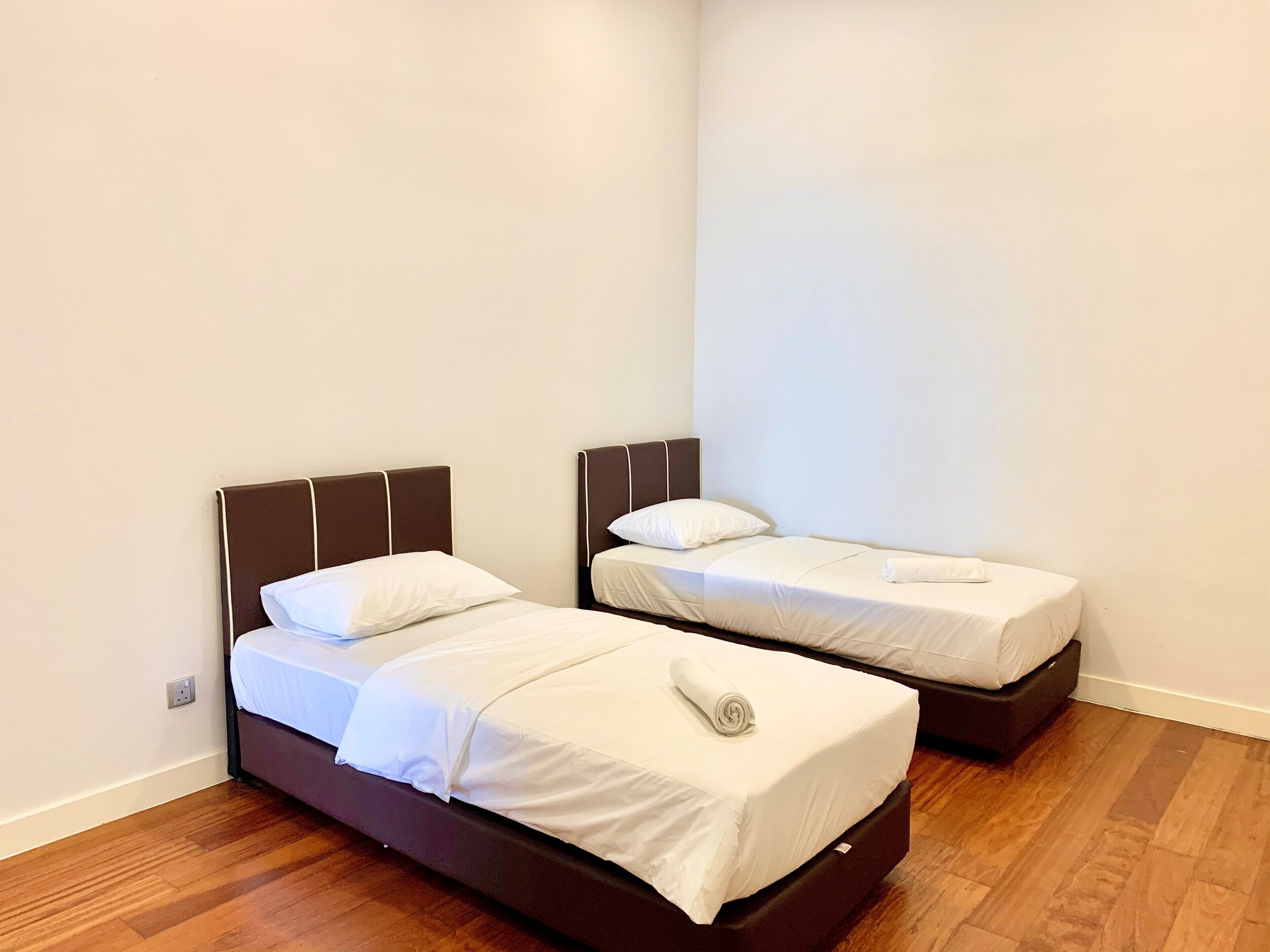 Dos camas individuales con cabeceros, ropa de cama blanca y suelo de madera.