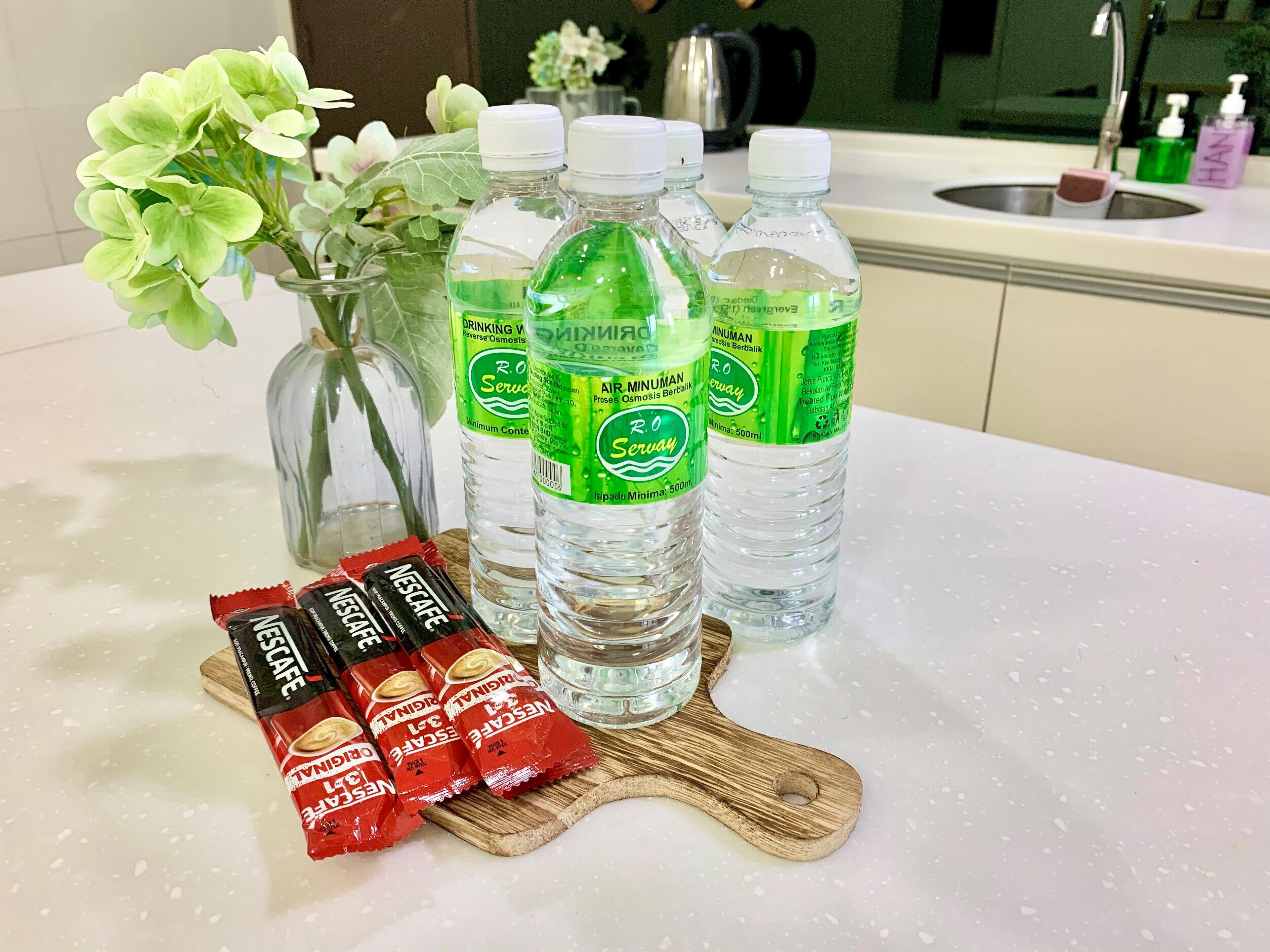 Un comptoir de cuisine avec des bouteilles d’eau, un vase rempli de fleurs et des sachets de café Nescafé.