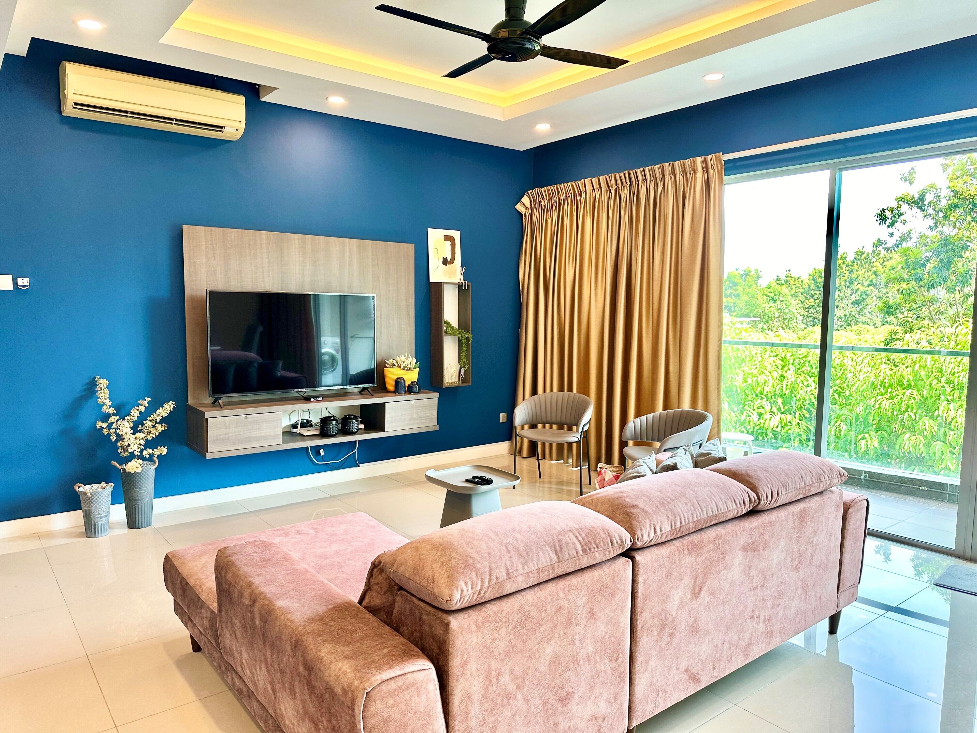 A modern living room with a large flat-screen TV, a ceiling fan, and a large window with curtains.
