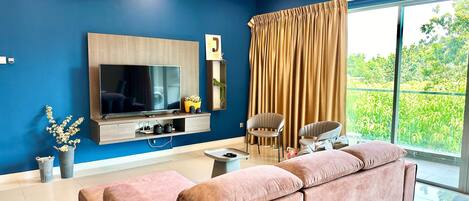 A modern living room with a large flat-screen TV, a ceiling fan, and a large window with curtains.