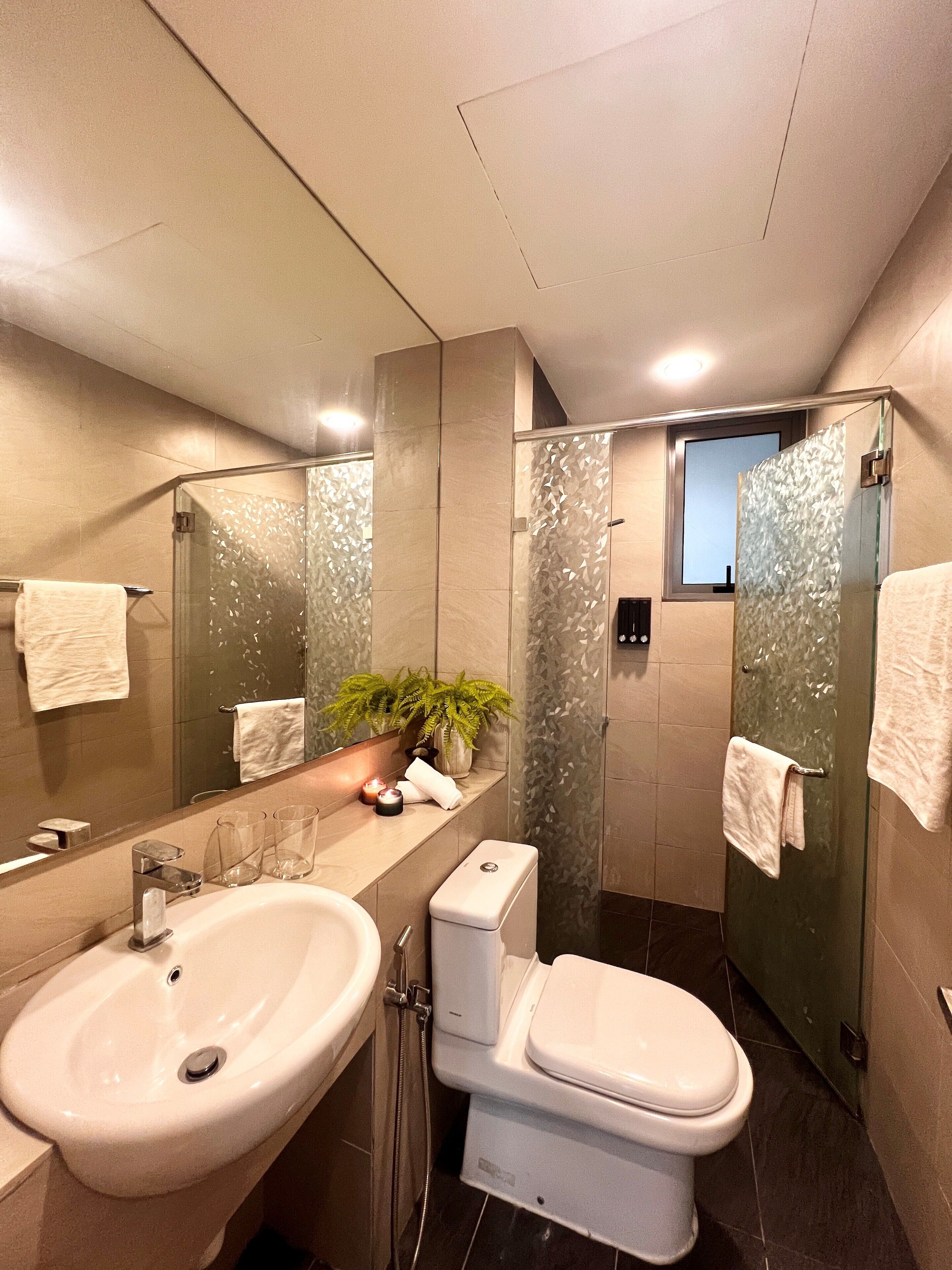 A modern bathroom with a large mirror, a sink, a toilet, and a glass-enclosed shower.