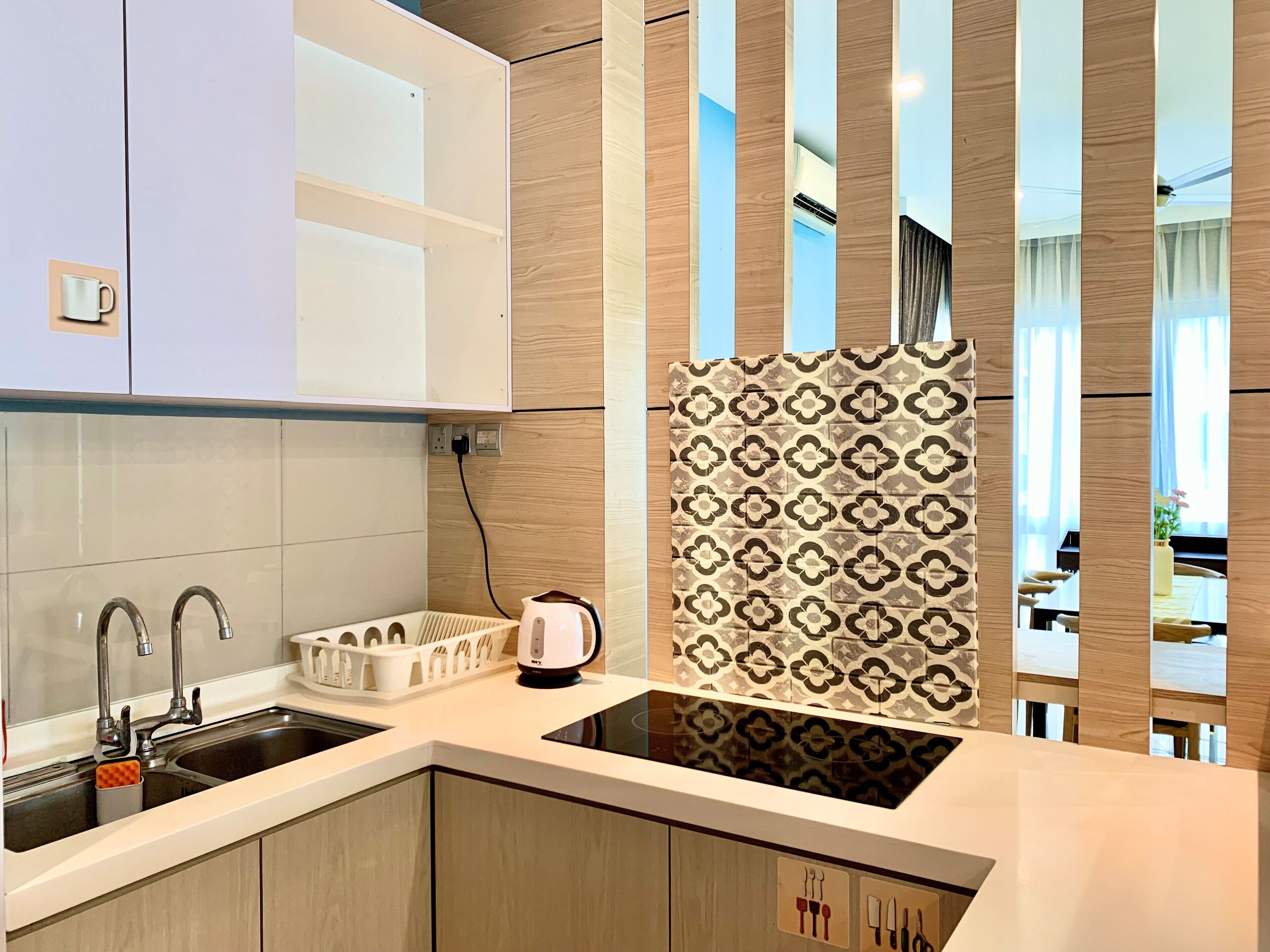 A modern kitchen with a built-in sink, a kettle, and a coffee maker. There is a wooden cabinet above the sink and a patterned backsplash.