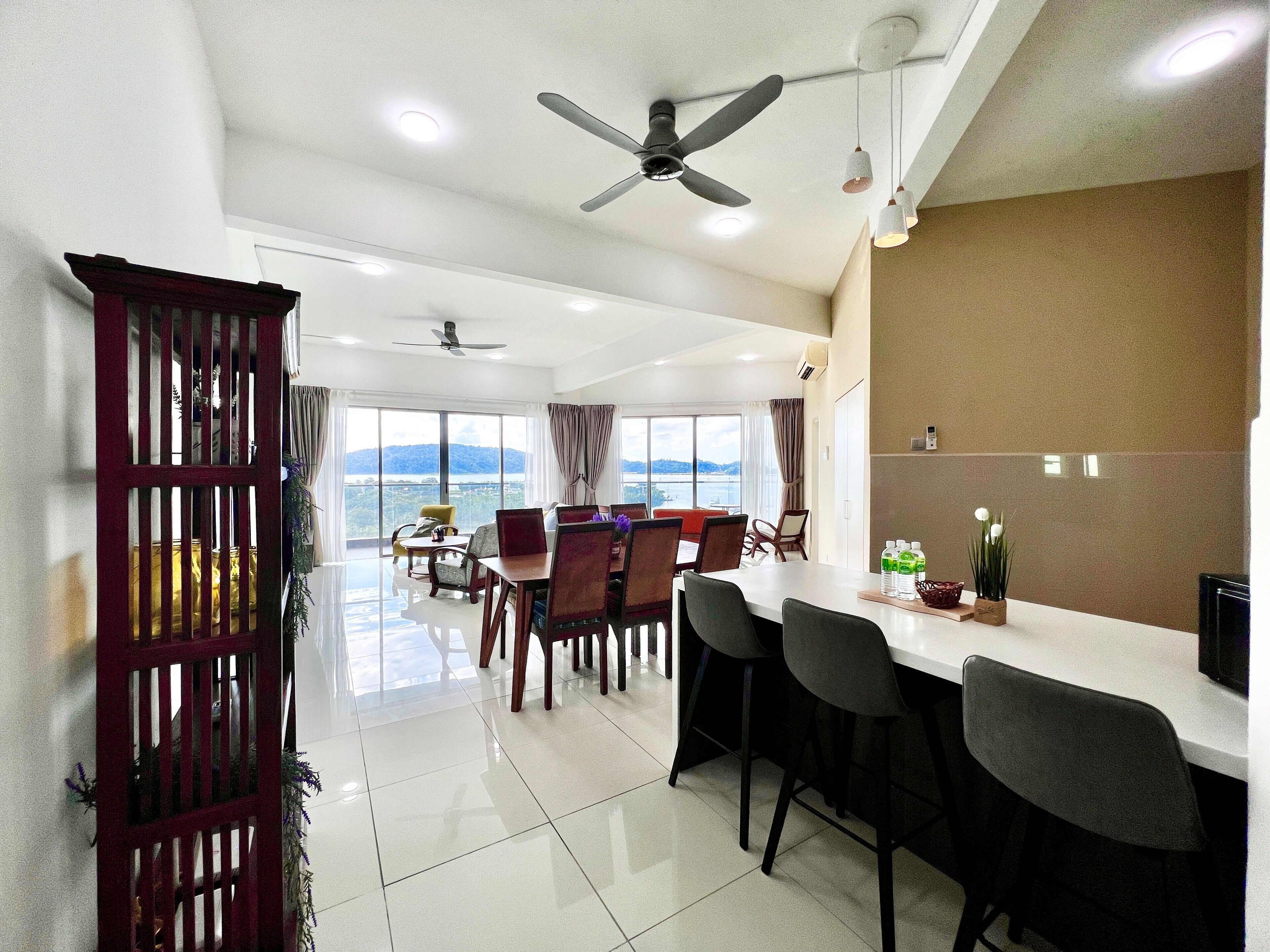 A modern hotel room with a dining area, large windows, ceiling fans, and a view of the mountains.