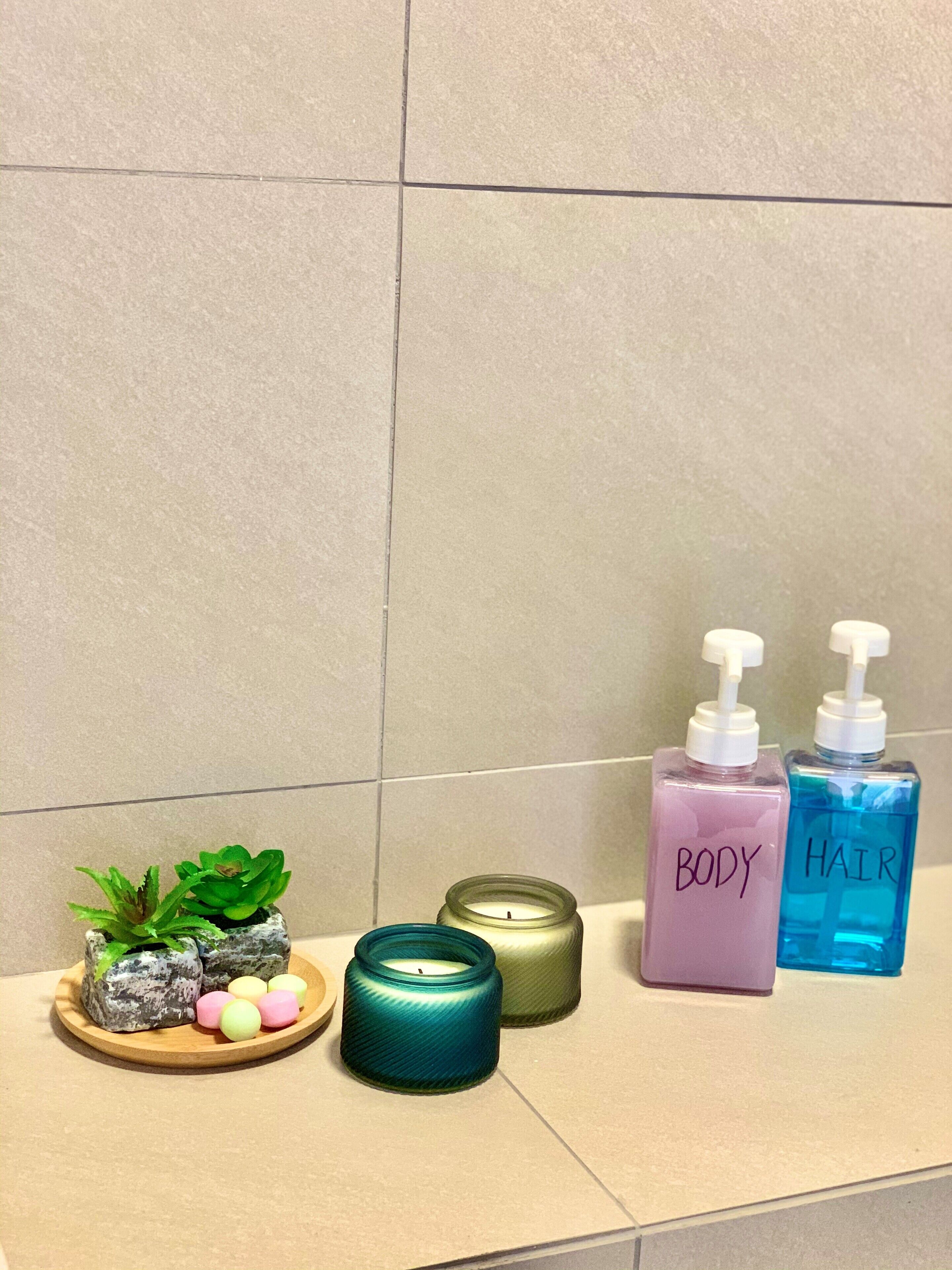 A bathroom shelf with a small plant, candles, and body and hair care products.