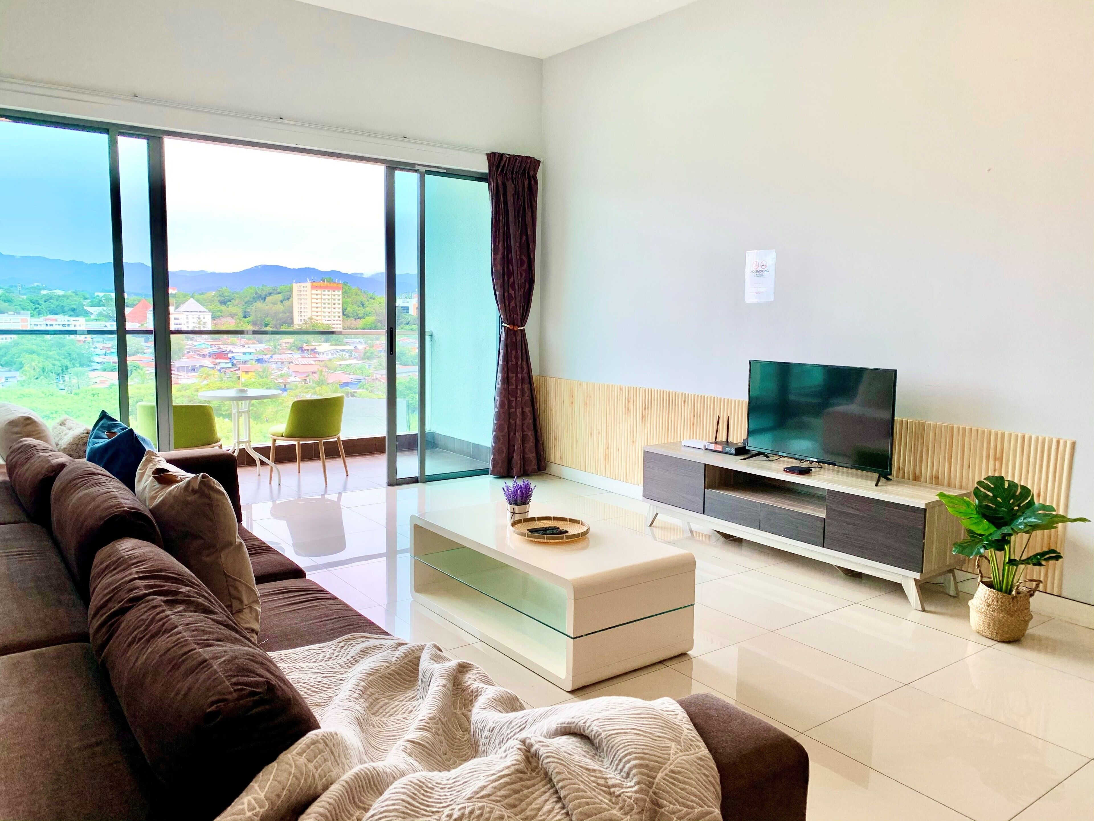 A modern living room with a large window, a sofa, a TV, and a small table.