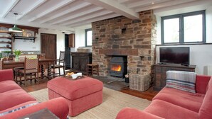 Una sala de estar acogedora con chimenea de piedra, mobiliario tapizado en rojo y un televisor.