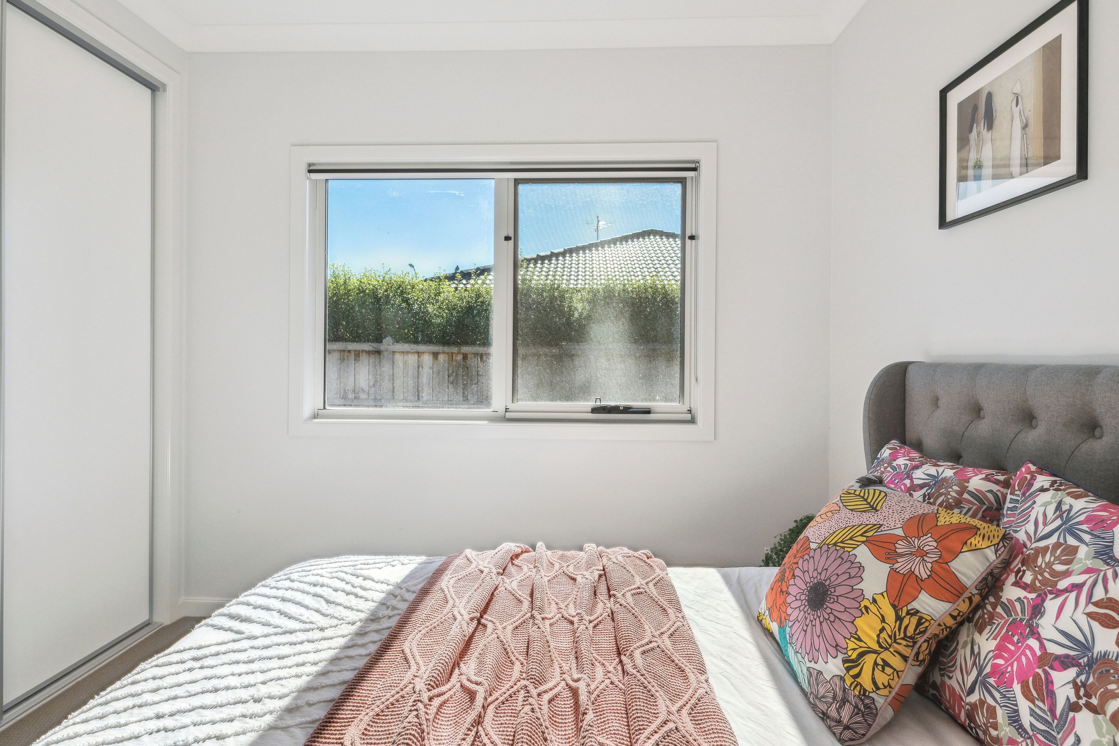 A bedroom with a bed, a window with a view of greenery, and a framed picture on the wall.