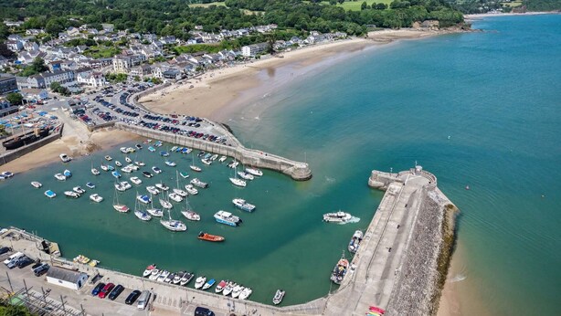 An aerial view of a coastal town with a marina, sandy beach, and residential area.