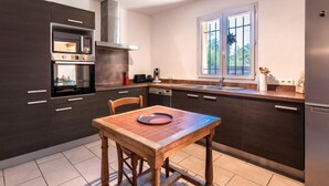 A modern kitchen with dark cabinetry, a wooden dining table, and a window with a view of greenery. - Casa Brigitte by Interhome (Pinarellu)