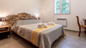 A bedroom with a bed, a nightstand, a chair, a window, and a wall-mounted heater. - Casa Brigitte by Interhome (Pinarellu)