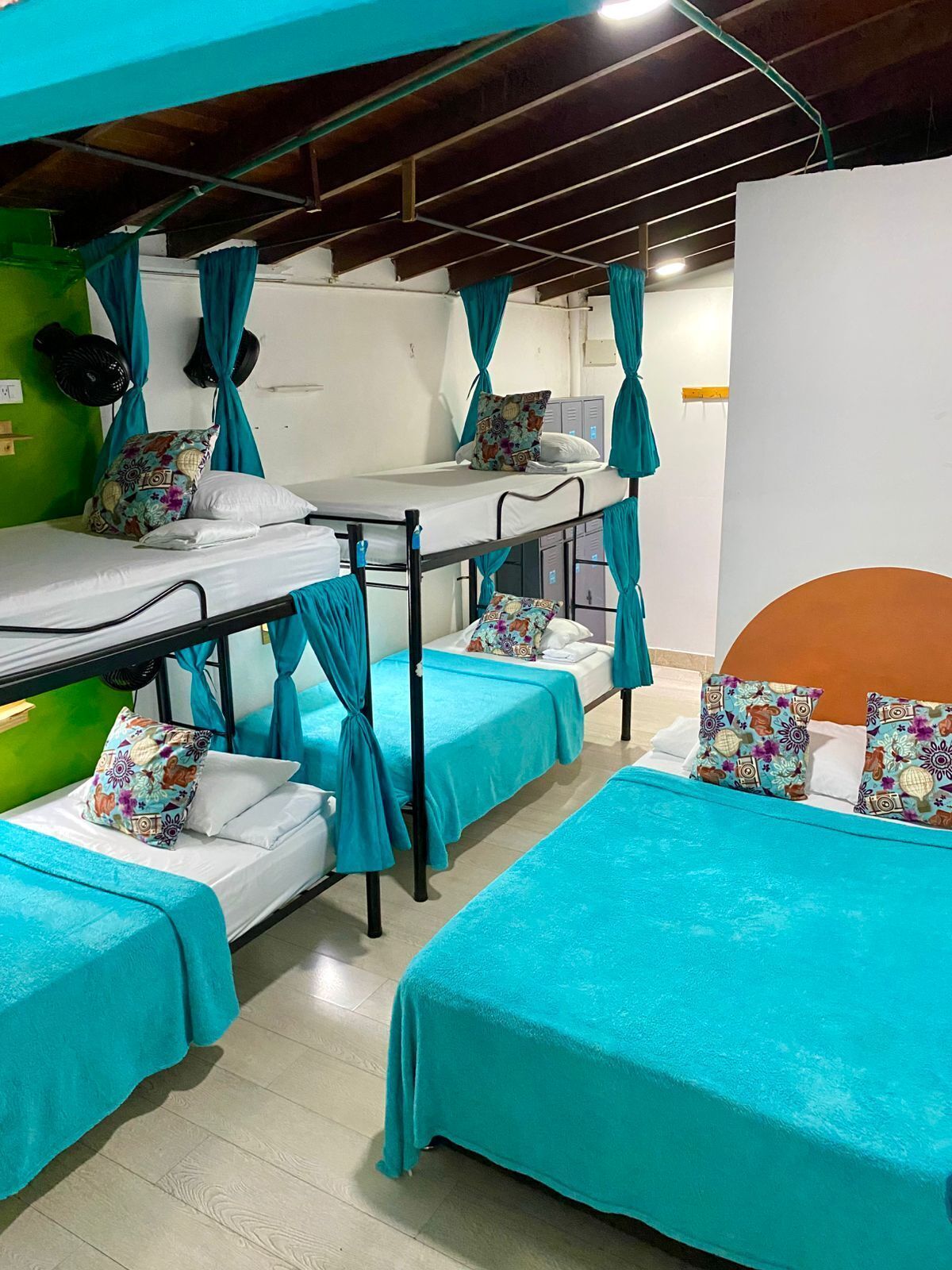 A dormitory with bunk beds and individual beds, each with a teal bedspread and patterned pillows.