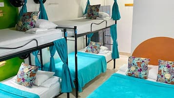 A dormitory with bunk beds and individual beds, each with a teal bedspread and patterned pillows.
