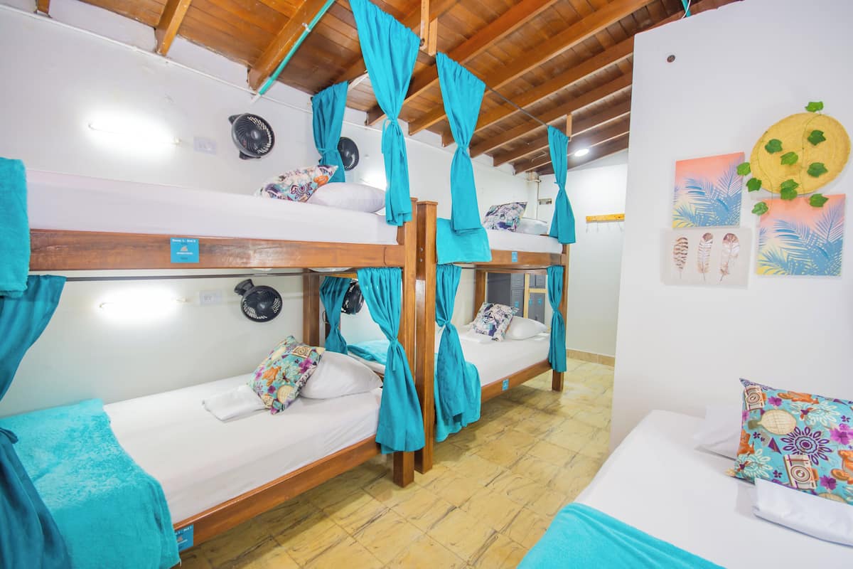 Quarto com beliches, cada um com cortina. Há ventiladores de parede e obras de arte nas paredes.
