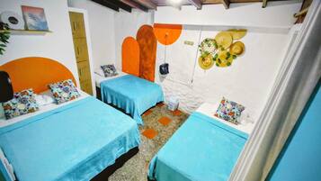Habitación con dos camas, techo de madera, pared blanca decorada con adornos naranja y amarillo, y una pequeña mesa con un cubo.