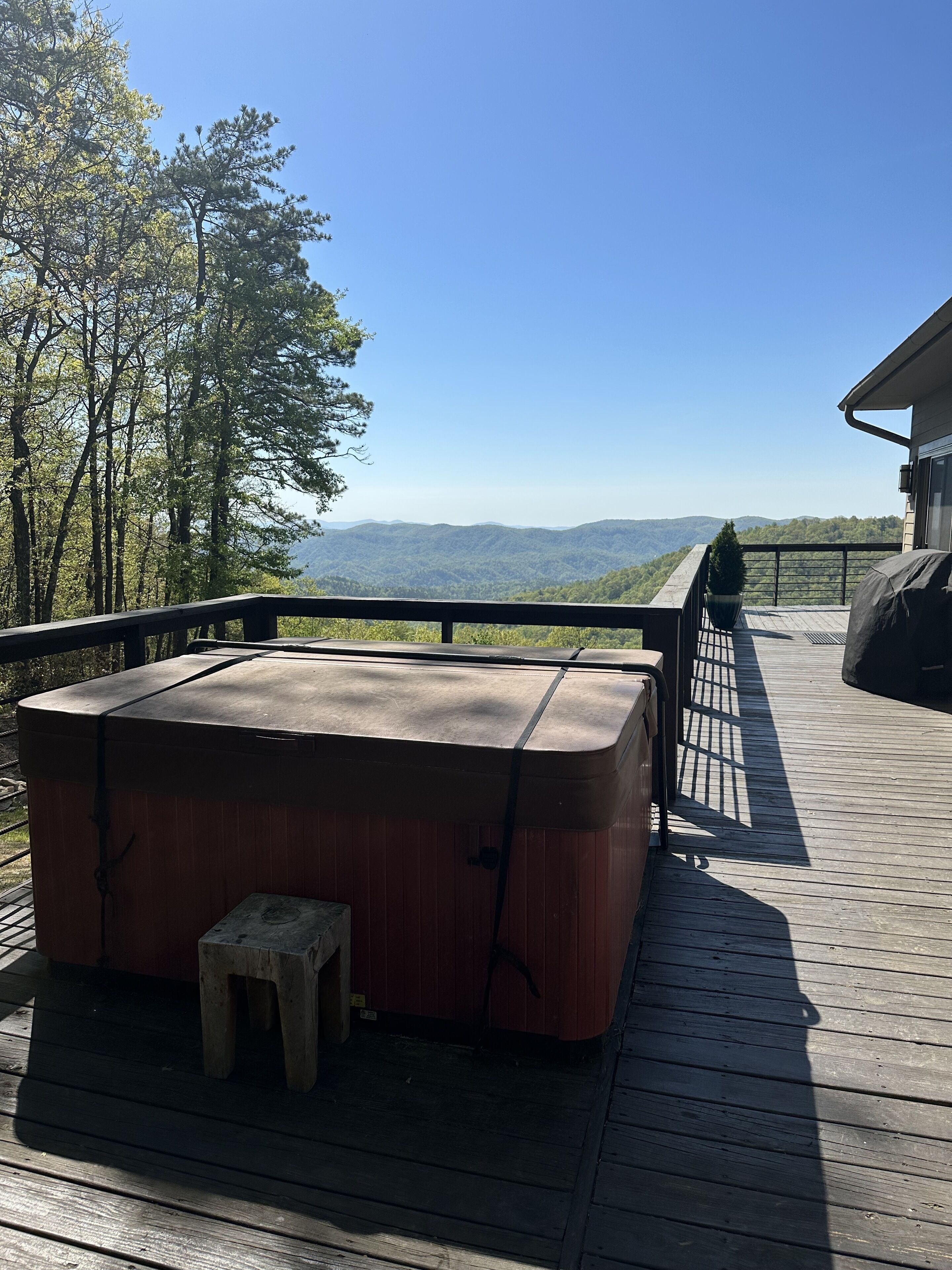 A wooden deck with a hot tub, a small stool, and a view of mountains.