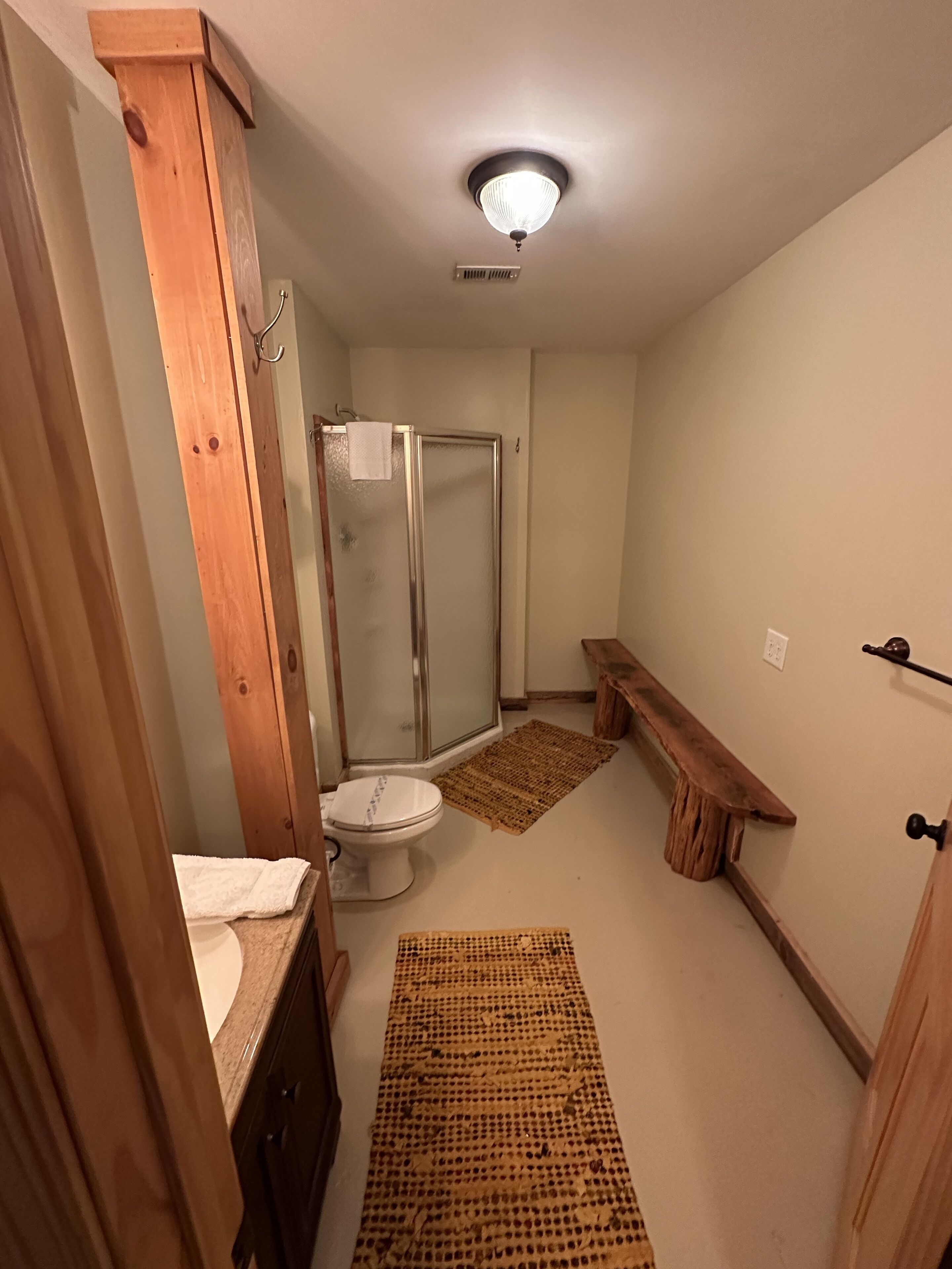 A bathroom with a toilet, shower, and wooden bench.
