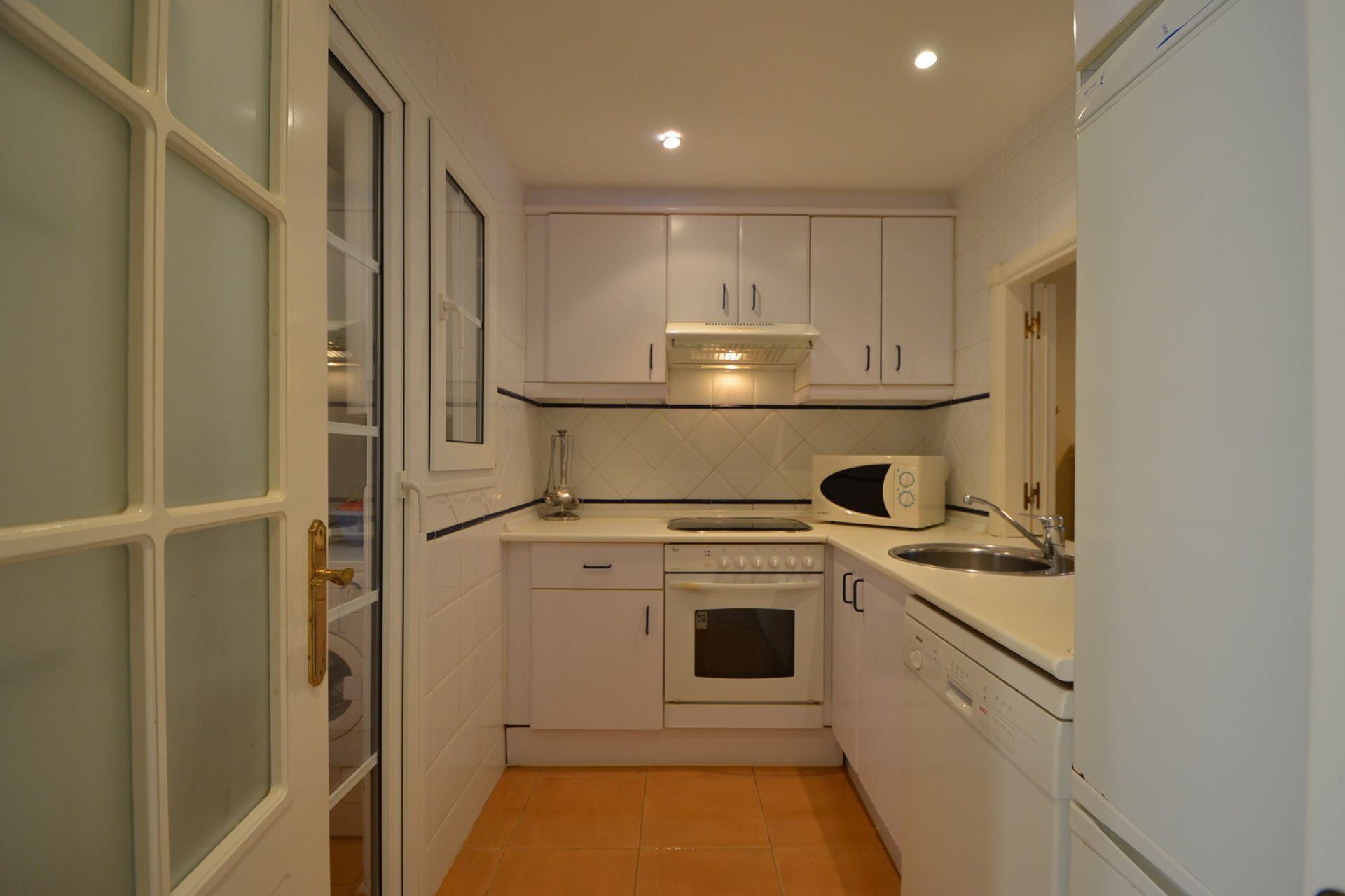 Une cuisine de taille réduite avec des meubles blancs, un four à micro-ondes, une cuisinière et un évier.