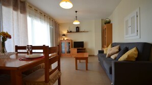 A living room with a dark-colored sofa, wooden dining table, chairs, and a television. - ESPIGÓN LEVANTE 8 - Two Bedroom Apartment, Sleeps 5 (Punta del moral)