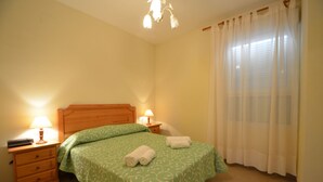 A bedroom with a wooden headboard, two bedside tables with lamps, a green patterned bedspread, and a window with sheer curtains. - ESPIGÓN LEVANTE 8 - Two Bedroom Apartment, Sleeps 5 (Punta del moral)