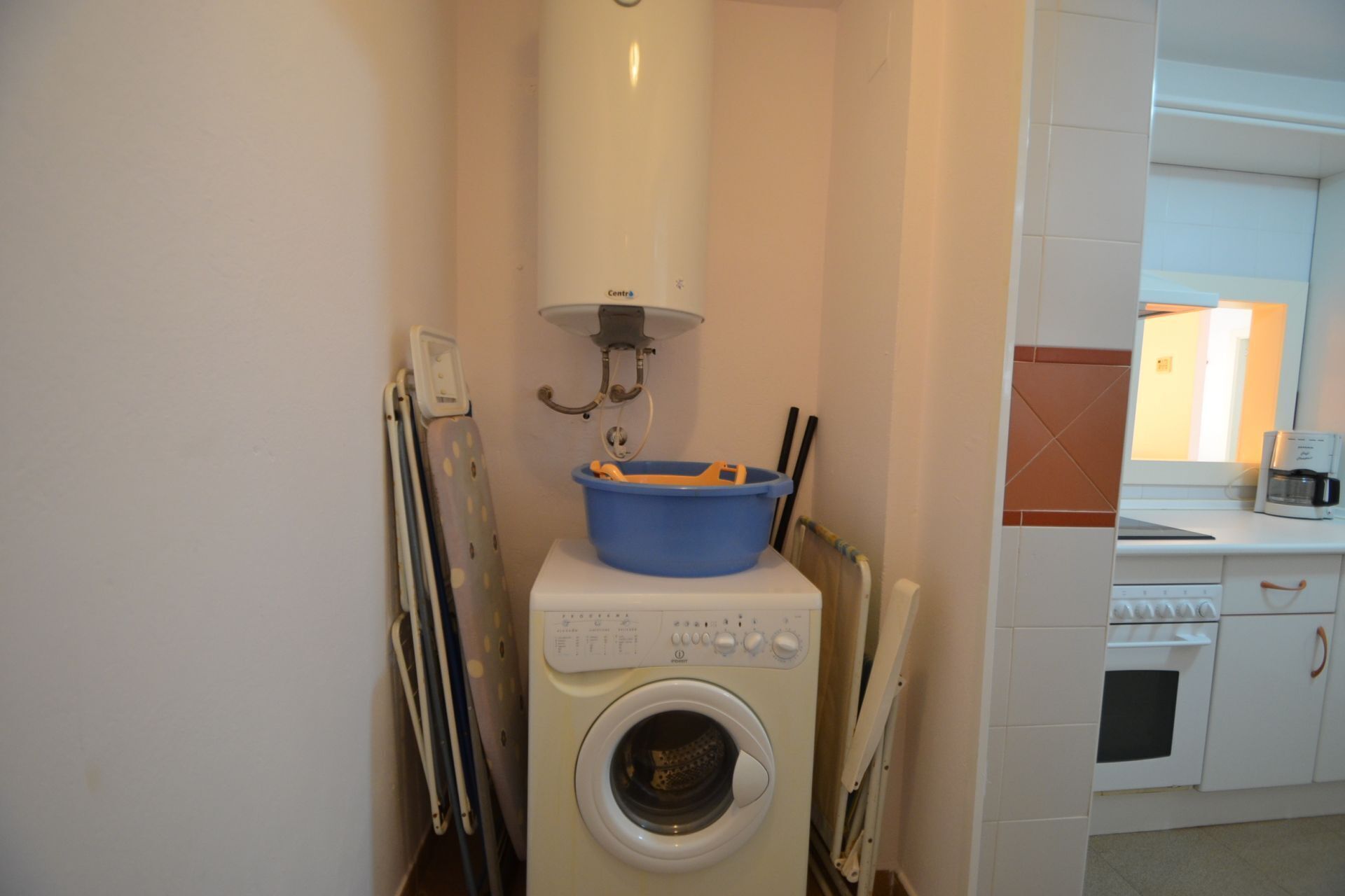 A compact laundry area with a washing machine, a drying rack, and a blue basin.