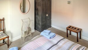 A bedroom with a bed, a chair, a small table, a wardrobe, and a mirror. - 3 bedroom accommodation in Sheringham (Sheringham)