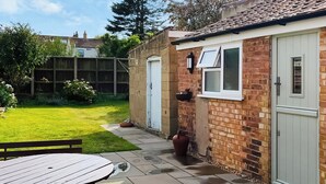 A patio with a table and chairs, a brick wall, a white door, and a small window. - 3 bedroom accommodation in Sheringham (Sheringham)