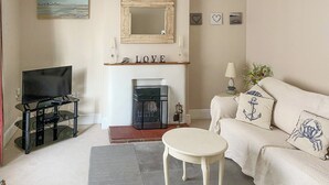 A living room with a fireplace, a television, a sofa, and a small table. - 3 bedroom accommodation in Sheringham (Sheringham)