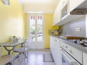 Cozinha compacta com área de jantar, apresentando uma mesa pequena, cadeiras e vista através de uma porta de vidro.