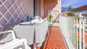Un balcón con una mesa para dos, sillas blancas, un mantel blanco y vistas a la ciudad y a las montañas.