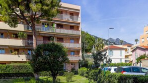 Un edificio residencial de varios pisos con balcones, rodeado de vegetación y automóviles estacionados.