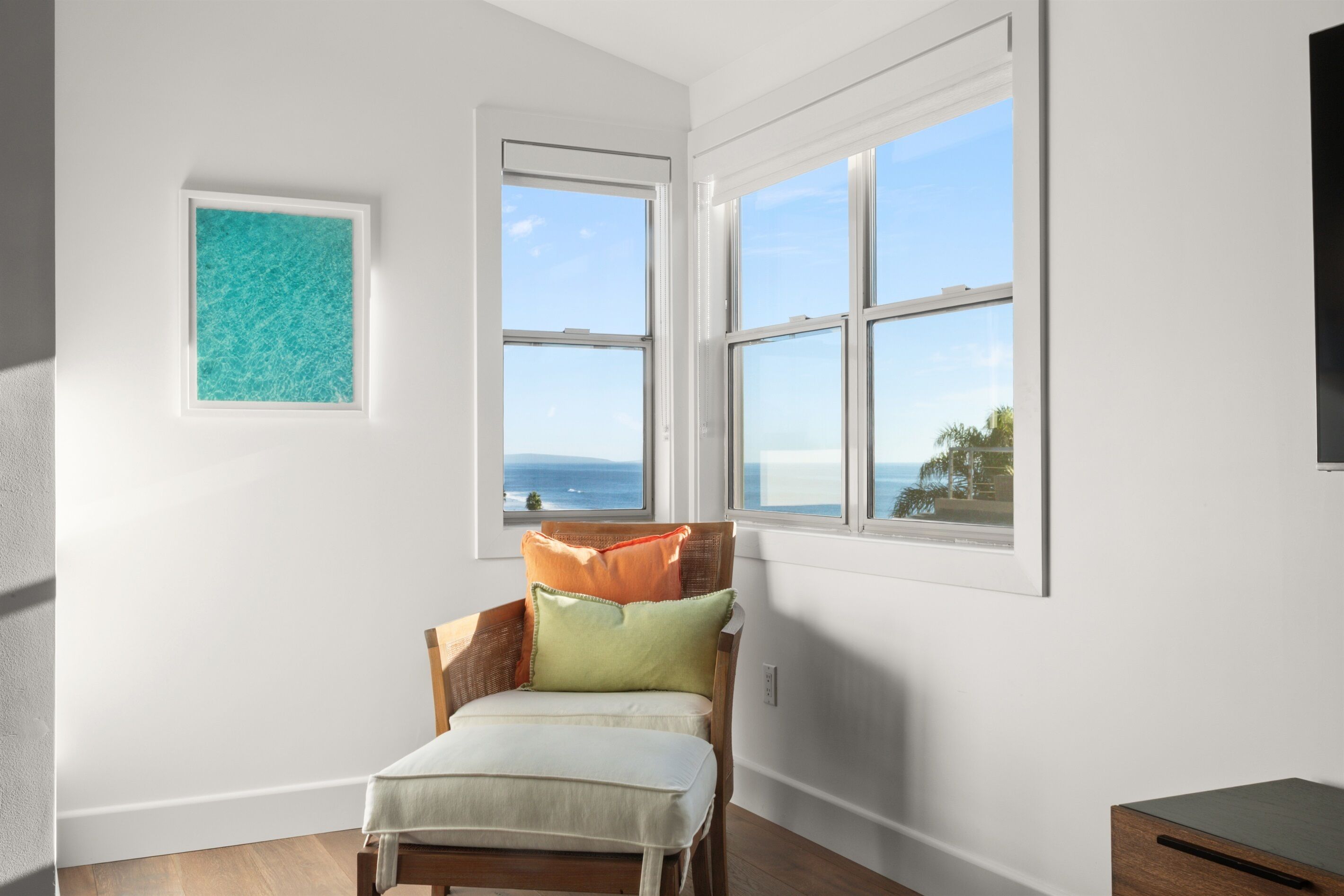 Une chambre avec vue sur l’océan, une œuvre d’art encadrée et un fauteuil avec des coussins.