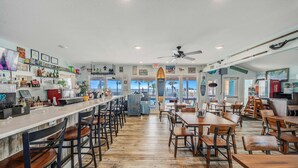 Un restaurant doté d’un bar, de tables et de chaises en bois, et offrant une vue sur la plage.