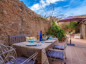 An outdoor dining area with a stone wall backdrop, a table set for two with blue glassware, and a purple umbrella. - Cas Moliner by Interhome (Petra)