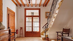 Una habitación amplia con una escalera de madera, una puerta grande de madera y piso de baldosas.