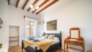 Un dormitorio con una cama, un aparador de madera, una silla verde, una ventana con cortinas y un cuadro en la pared.