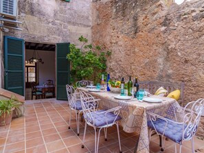 An outdoor dining area with a stone wall backdrop, a tiled floor, and a table set with chairs and bottles. - Cas Moliner by Interhome (Petra)