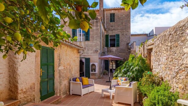 Un patio con mobiliario exterior, un muro de piedra y un edificio con contraventanas verdes.